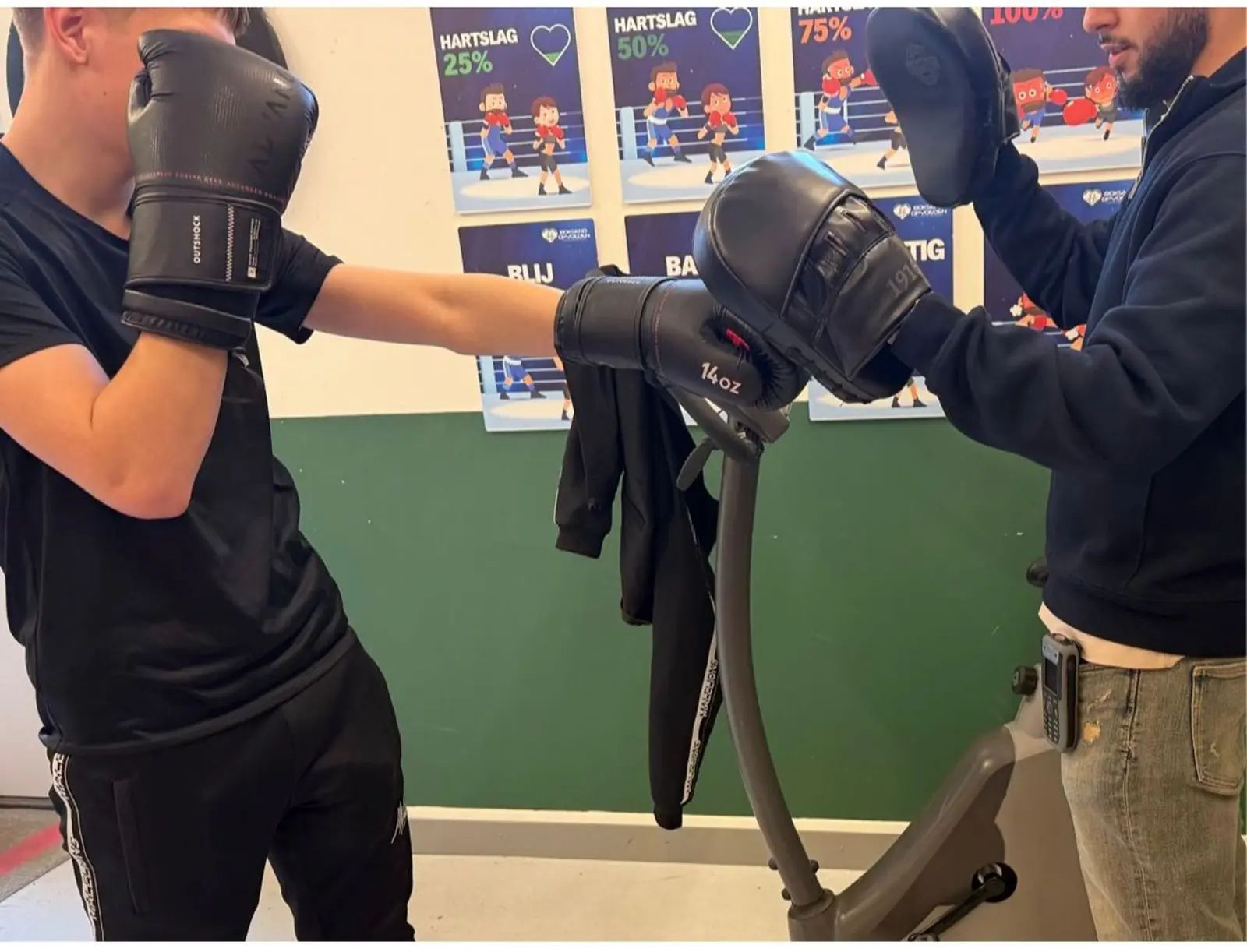 Jongere oefent boksen met begeleider met focuspads bij de Boksend Opvoeden-posters in de Novara-locatie