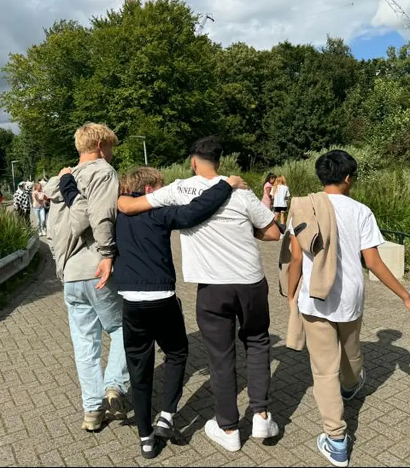 Drie jongeren en een begeleider lopen samen, arm om schouder, buitenlocatie. Eén plan, één betrokken netwerk.